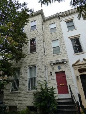 A white building with a red door and a black staircase.