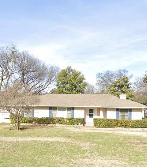 A white house with a brown roof and a tree in front.
