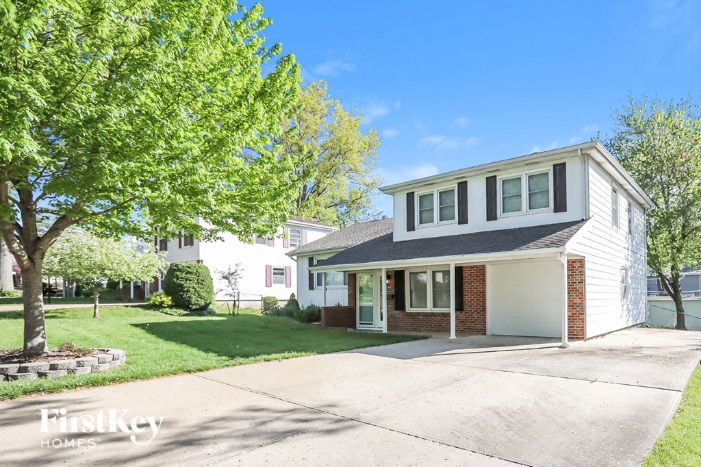 a white house with a driveway and a tree in front of it