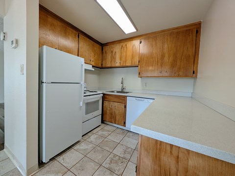 A kitchen with a white refrigerator, wooden cabinets, and a white countertop.