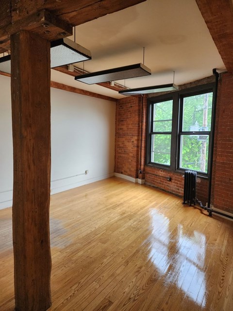 A room with wooden floors and a large window with a view of trees outside.