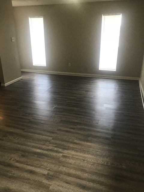 an empty living room with wood floors and two windows