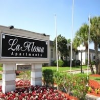 A sign for La Floresta Apartments is displayed in front of a building.