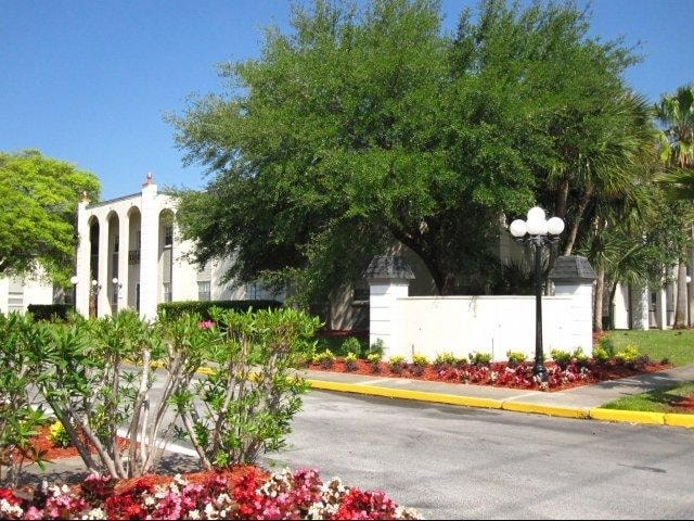 A white building with columns is surrounded by green trees and bushes.