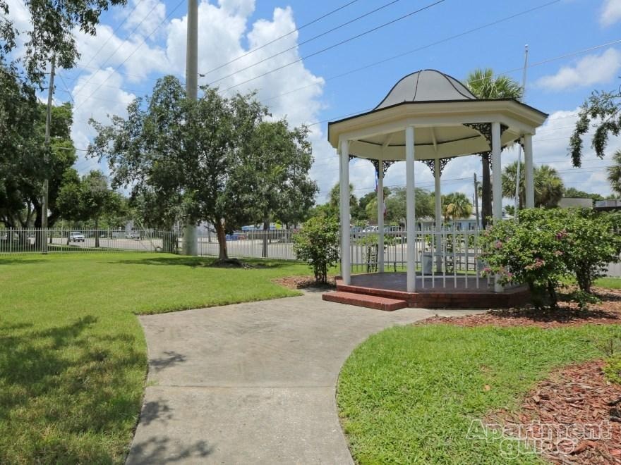 A gazebo is surrounded by a grassy area and a concrete walkway.