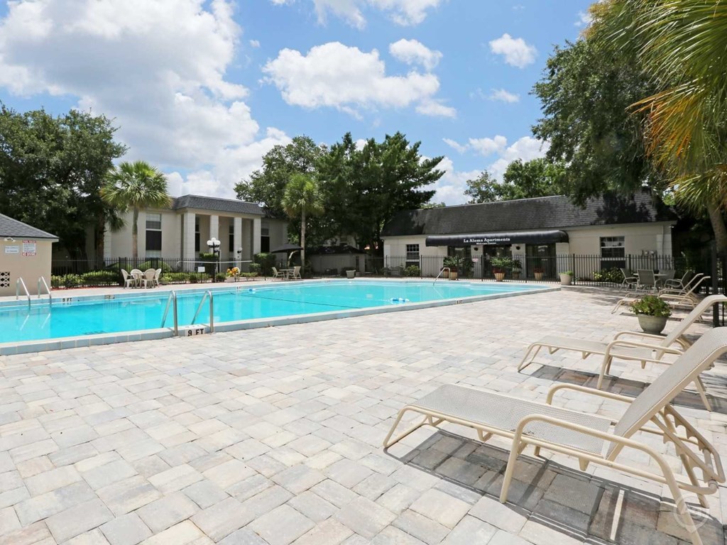 A pool surrounded by lounge chairs and trees.