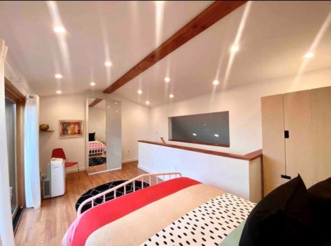 A bedroom with a red and white bed and a television on the wall.