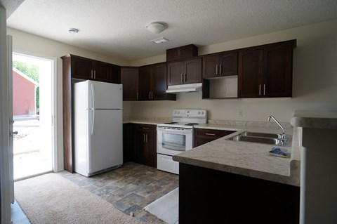 an empty kitchen with white appliances and dark cabinets