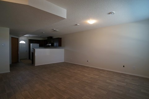 A large empty room with wooden floors and a kitchen area in the background.