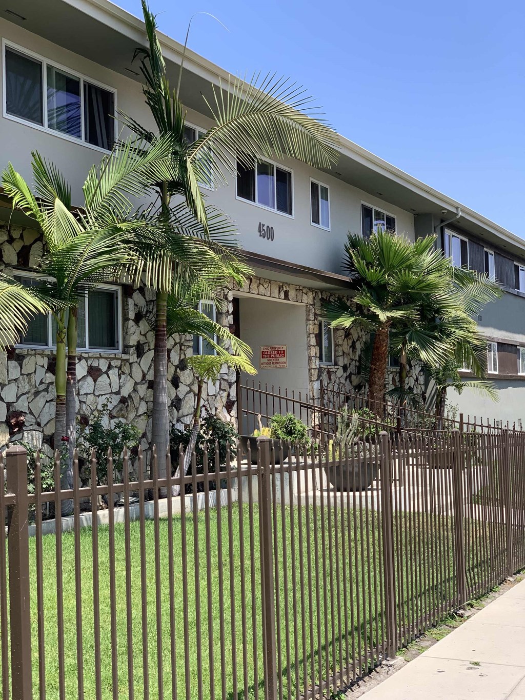 a house with a fence and palm trees in front of it