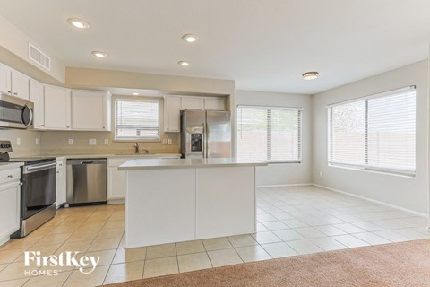 A kitchen with white cabinets and appliances, a brown rug on the floor, and a window with blinds.