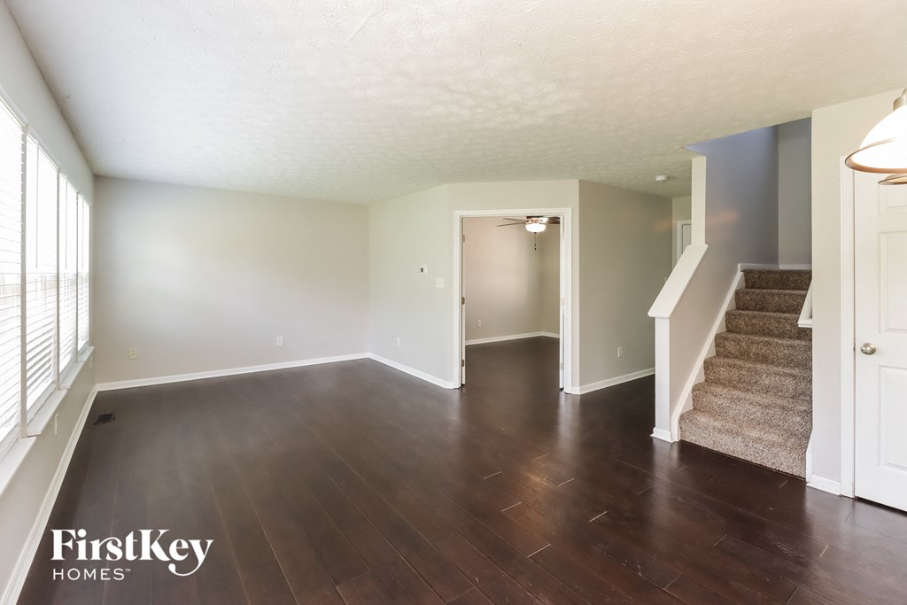 A spacious room with wooden floors and a staircase leading to another room.