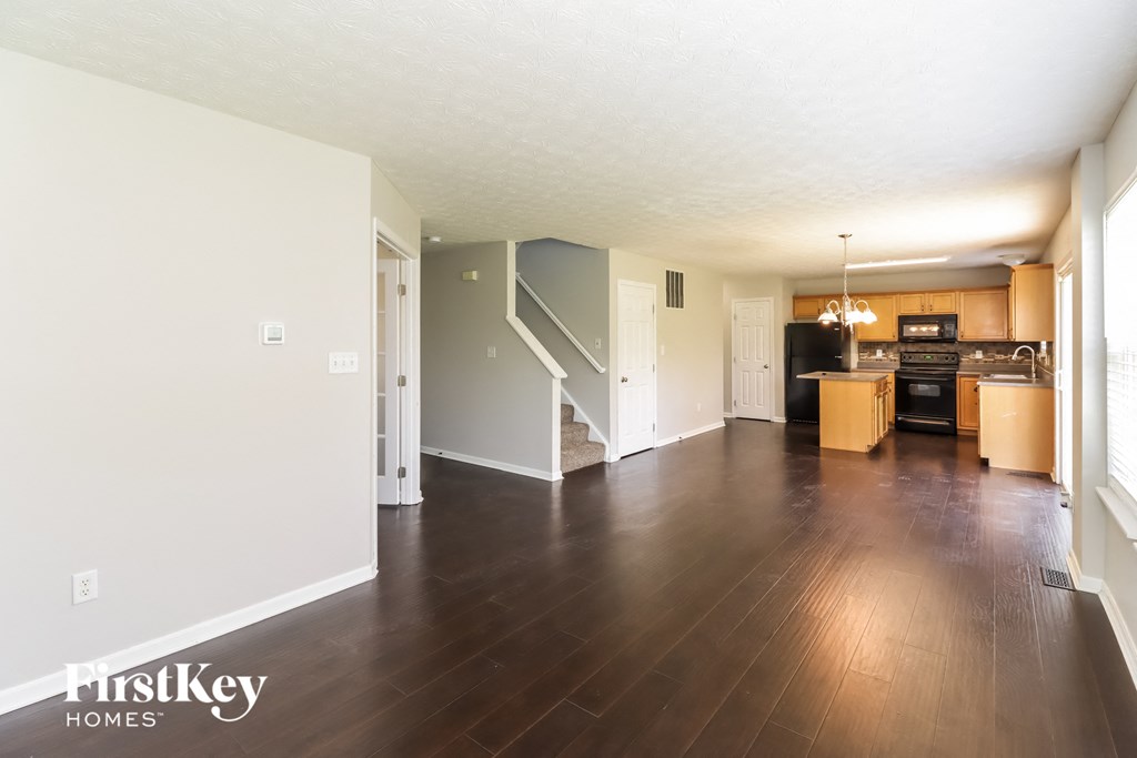 A spacious living room with wood flooring and a staircase in the background.