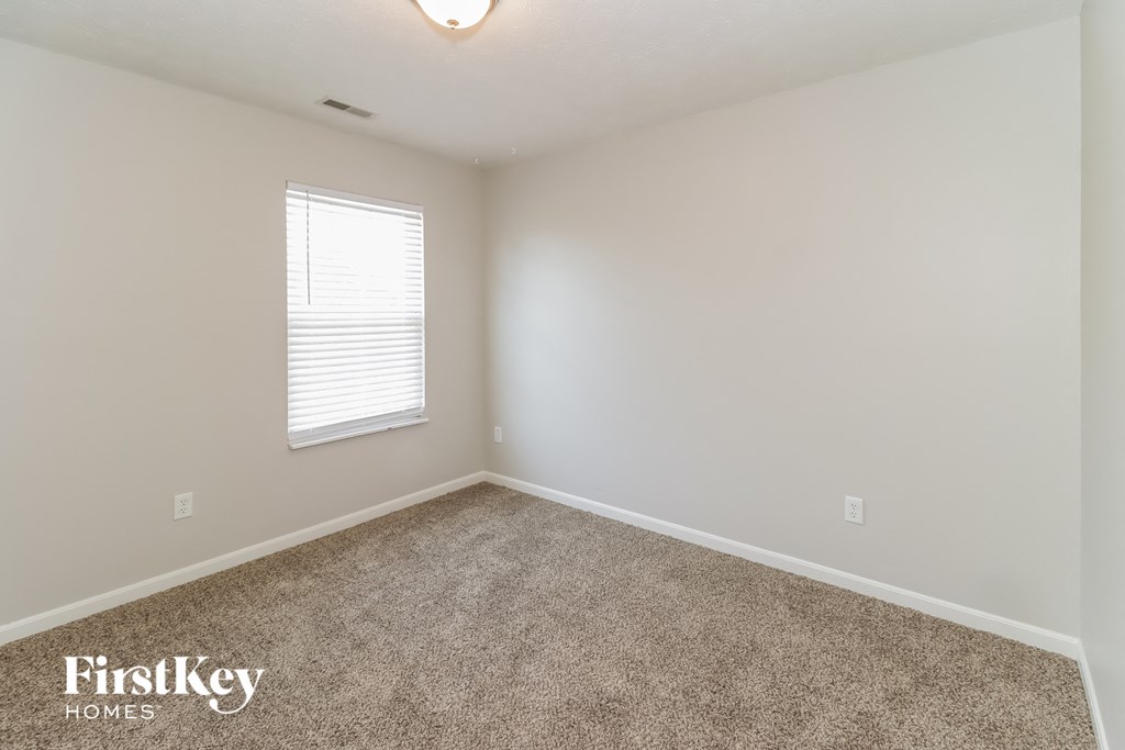 A room with a carpeted floor and a window with blinds.