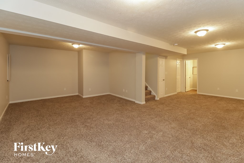 A spacious room with beige carpeting and white walls, with a staircase leading to another room.