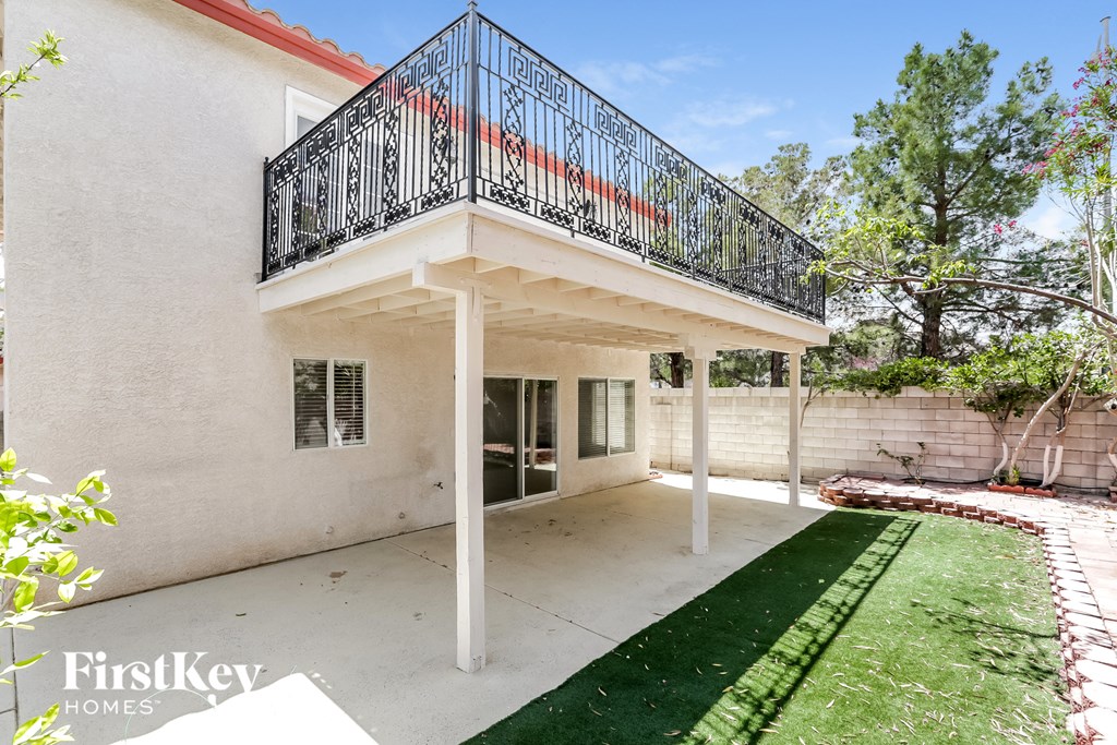 a patio with a green lawn and a white house with a balcony