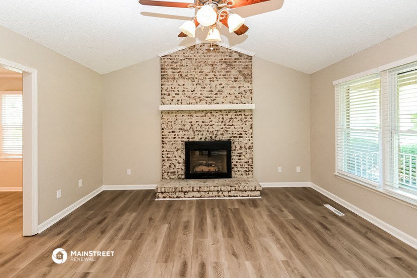 an empty living room with a brick fireplace and a ceiling fan