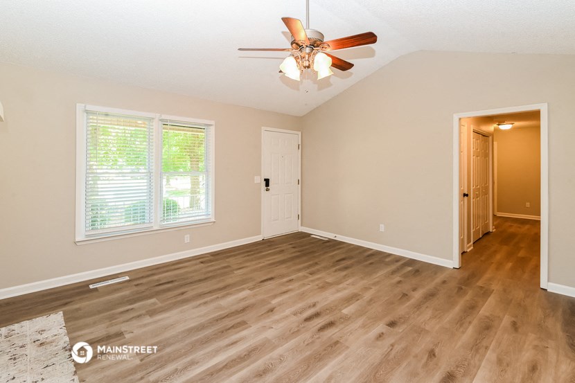 the spacious living room with hardwood flooring and a ceiling fan