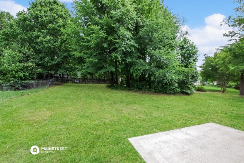 a backyard with grass and trees and a batting cage