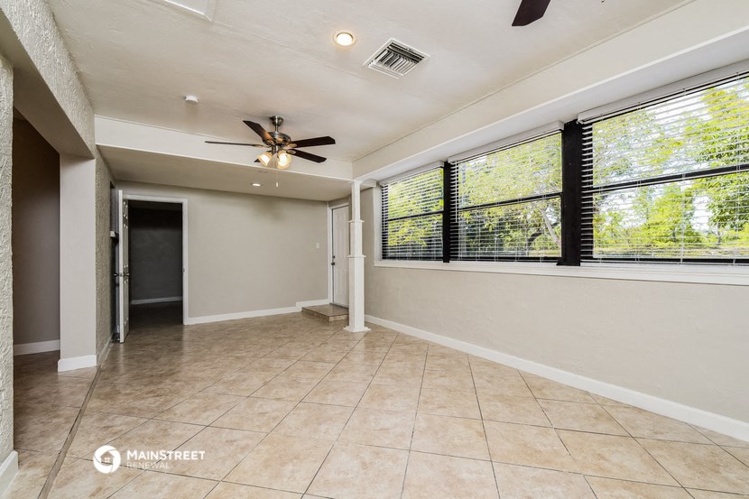 an empty living room with large windows and a ceiling fan