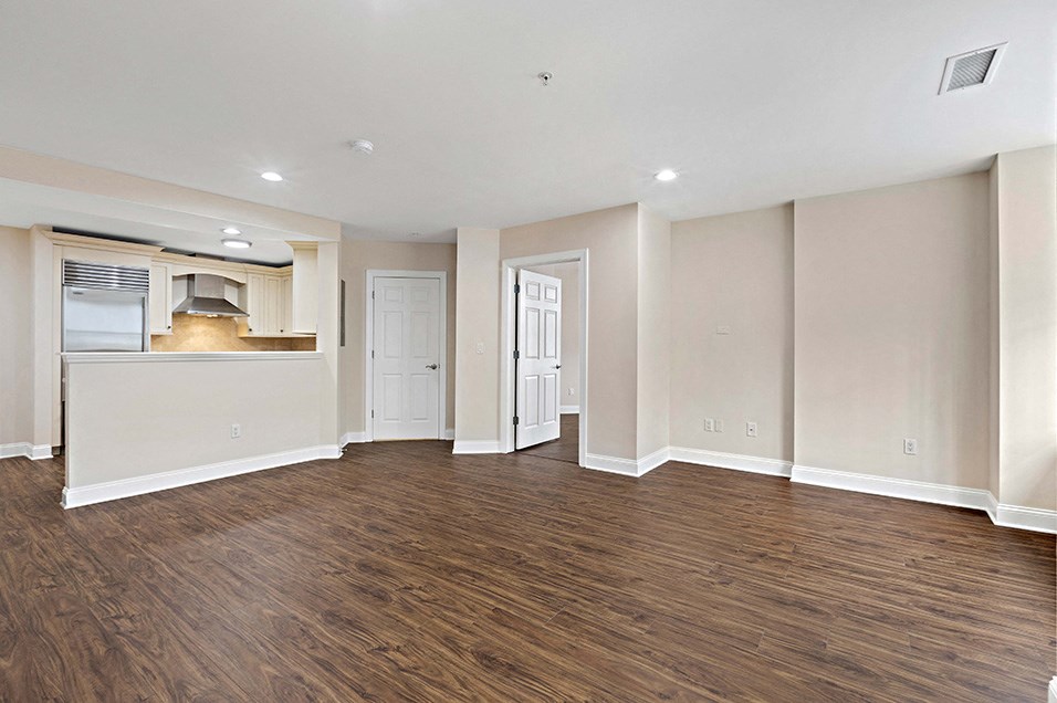an empty living room with wood flooring and a kitchen