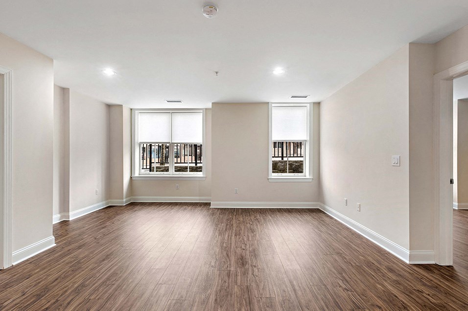 an empty living room with wood flooring and two windows