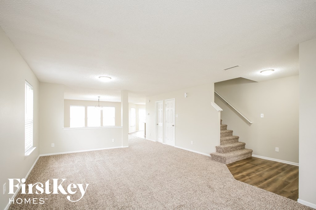 a spacious living room with carpet and stairs in a white house