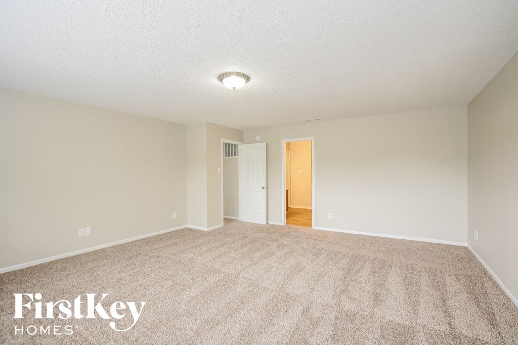 a spacious living room with carpet and a door to a hallway