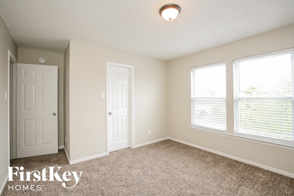 a bedroom with a carpeted floor and a door and two windows