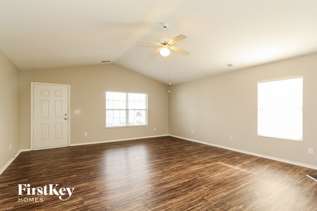 the spacious living room with hardwood flooring and a ceiling fan