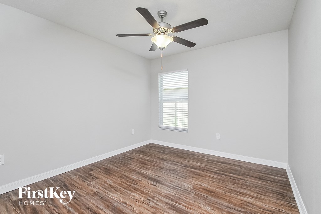 the spacious living room with wood flooring and a ceiling fan