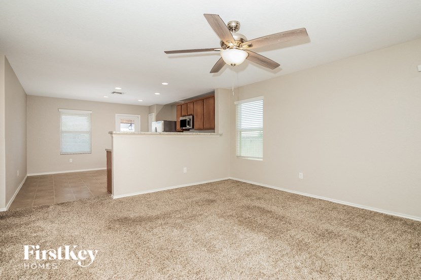 an empty living room with a ceiling fan and a kitchen