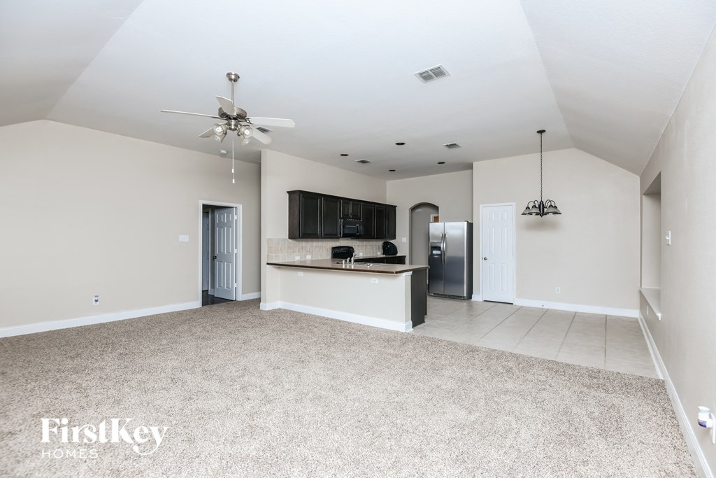 a spacious living room with a kitchen and a ceiling fan