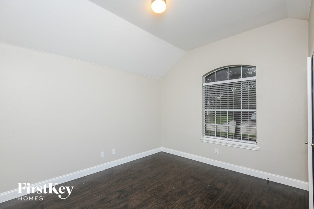 a bedroom with white walls and wood flooring and a window