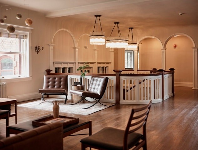 A living room with a brown leather chair and a white chair with a wooden table and a fireplace.