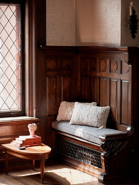 A wooden bench with a pillow and a stack of books on a table.
