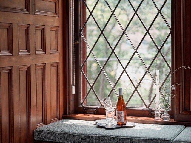 A bottle of wine sits on a table in front of a window.