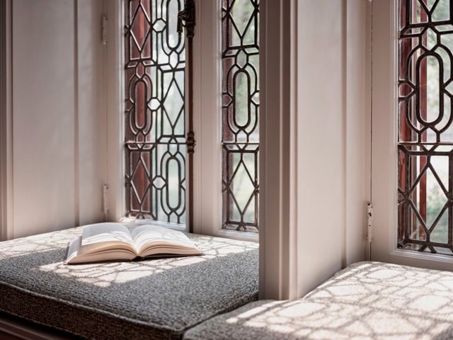 A book is open on a bed in front of a window with stained glass.