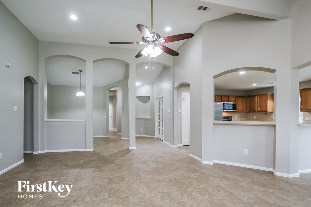 an empty living room with a ceiling fan and a kitchen
