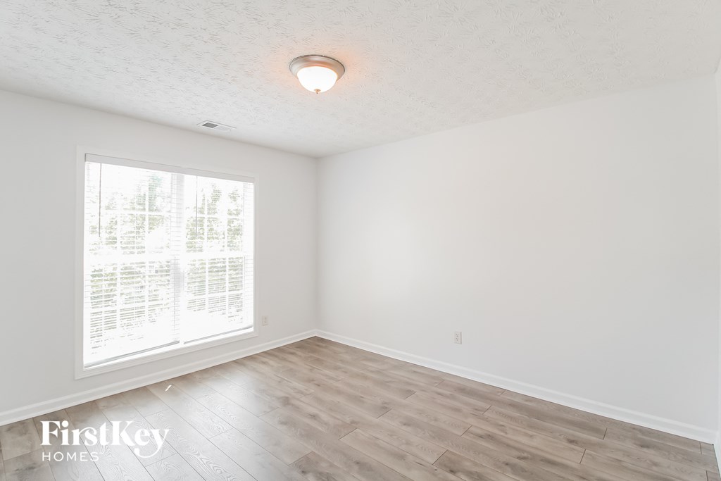 a bedroom with white walls and wood floors and a large window