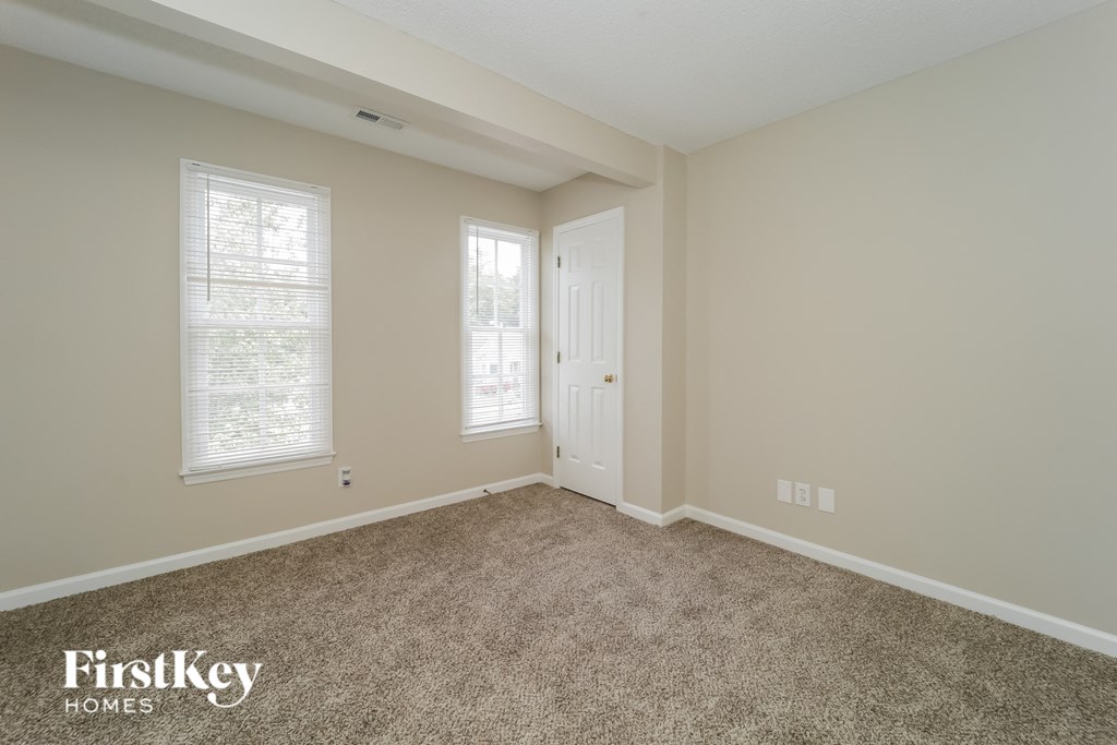 a carpeted room with a door and two windows