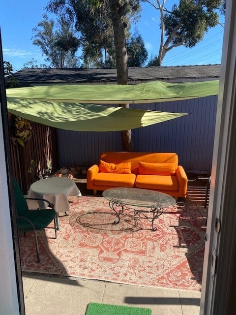 A patio with a green umbrella, orange couch, and a rug.