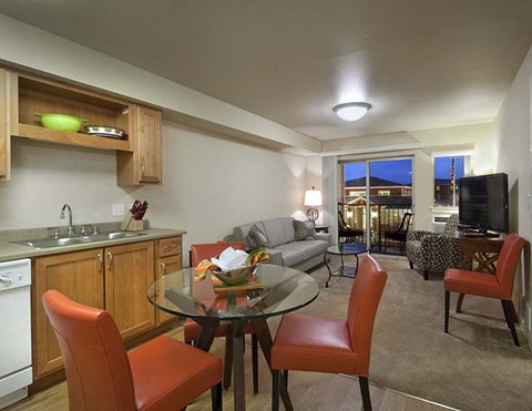 A kitchen with a table and chairs in the foreground and a balcony with a couch and chairs in the background.