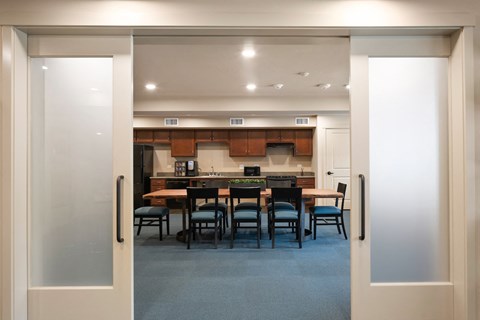 A modern kitchen with a dining table and chairs is visible through an open door.