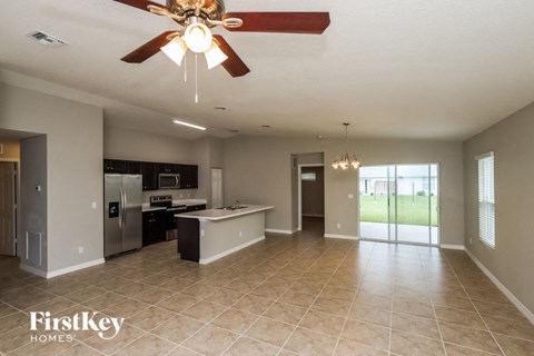 A spacious kitchen and living room with a ceiling fan and tiled flooring.