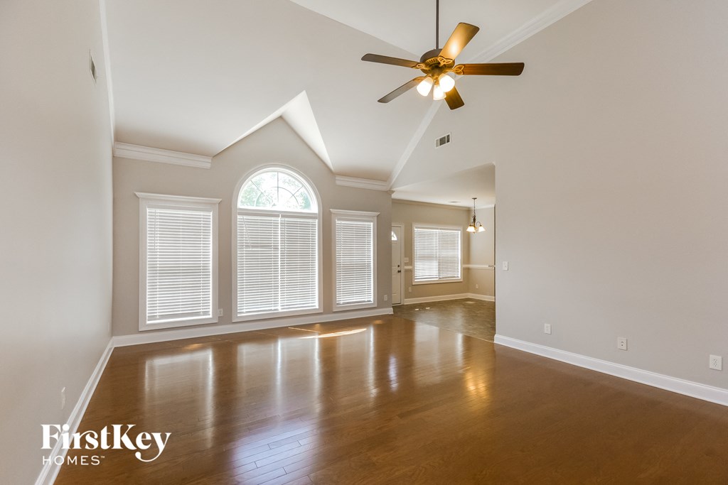 an empty living room with a ceiling fan and large windows