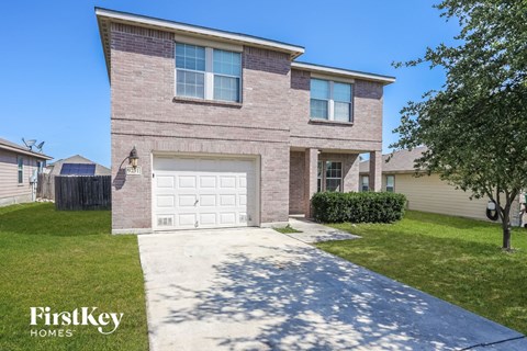 A brick house with a garage door and a tree in front.