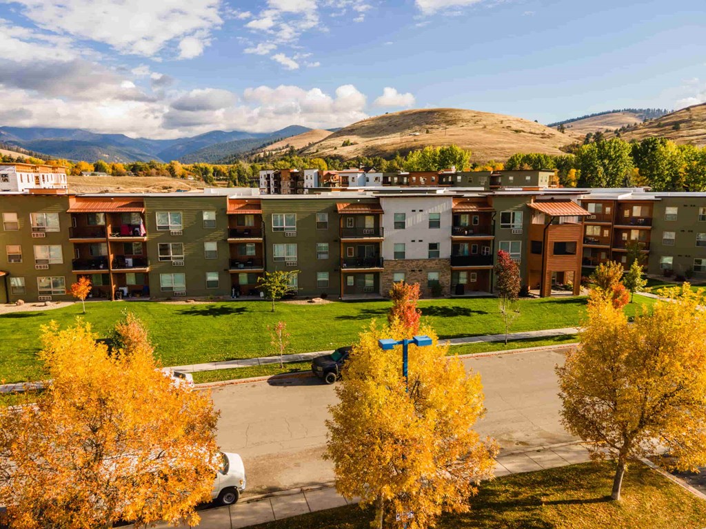 A view of apartment buildings with a car and trees in the foreground.
