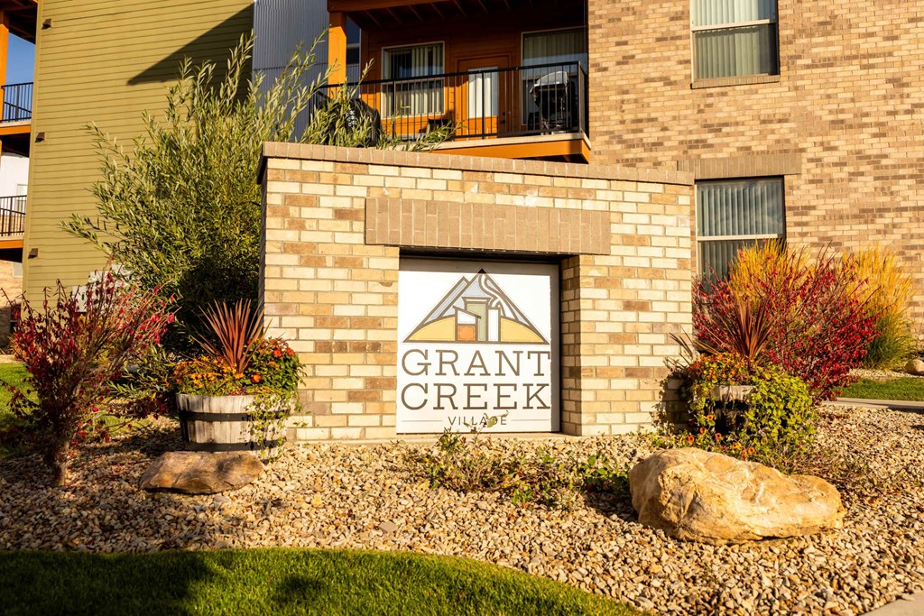 A sign that says "Grant Creek" is on a brick wall.