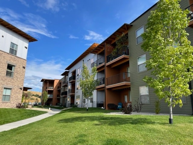 A tree stands in front of a tan building with a balcony.